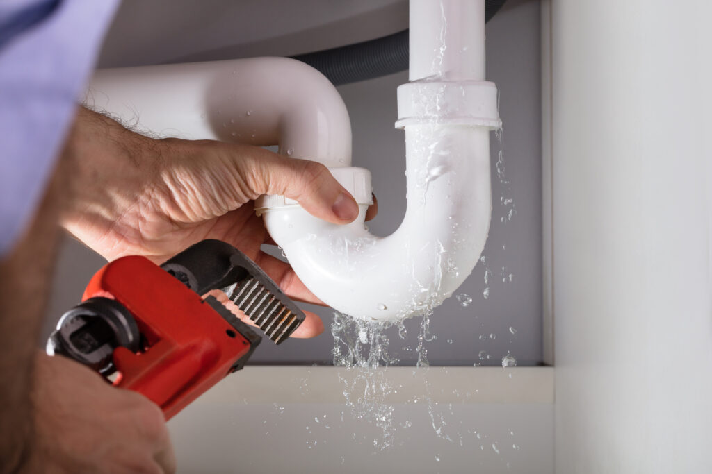 Close-up of male plumber fixing white sink pipe with adjustable wrench