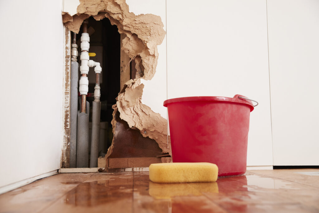 Damaged wall with exposed burst water pipes next to a sponge and bucket