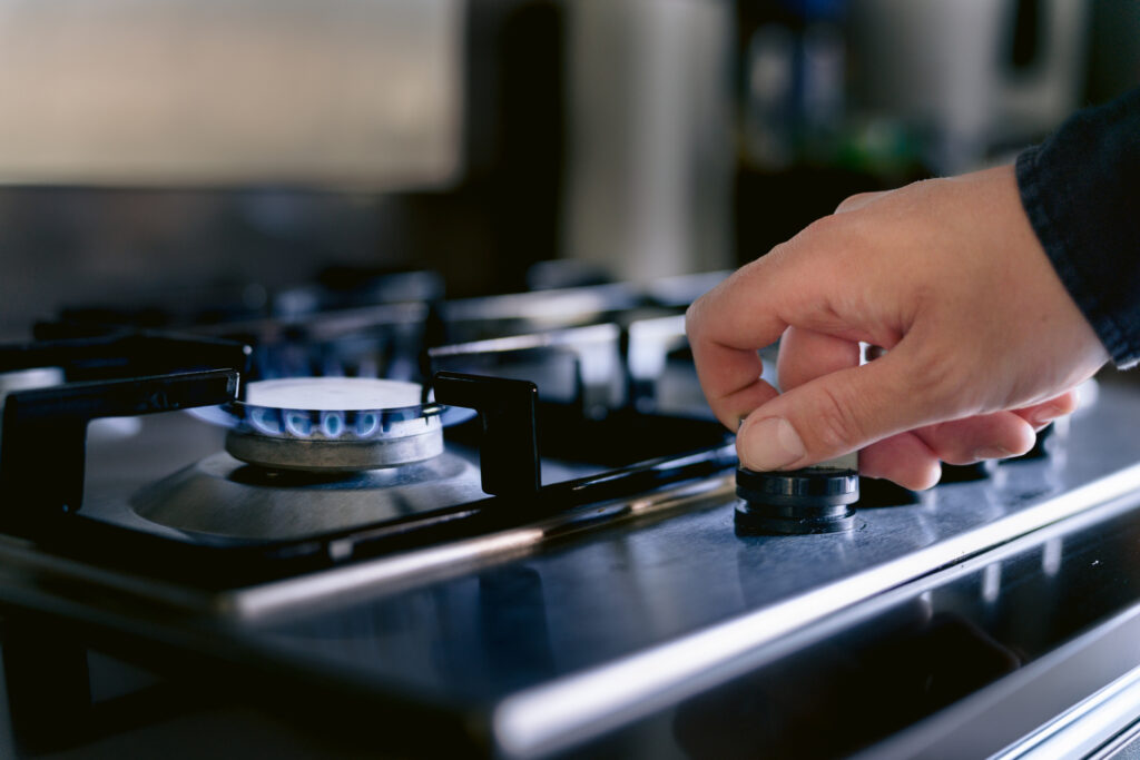 A hand turns on a stove fired by natural gas