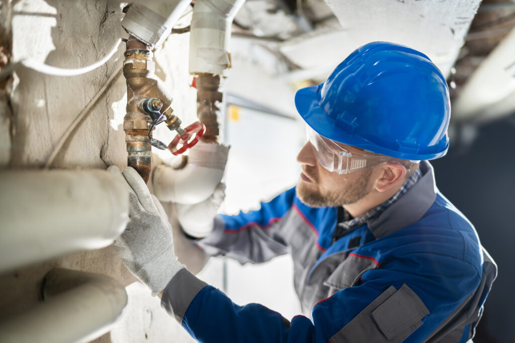 Plumber inspecting water valve for leaks in commercial basement