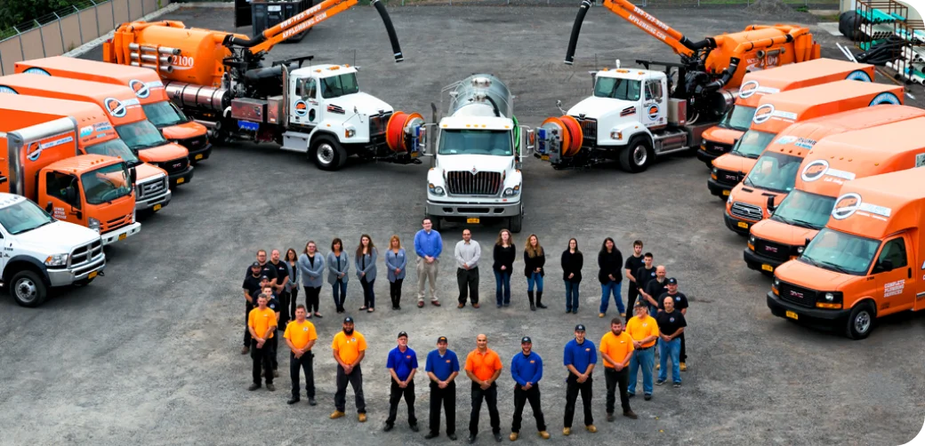 AP Plumbing team standing in a circle on black top in the middle of all the service vehicles