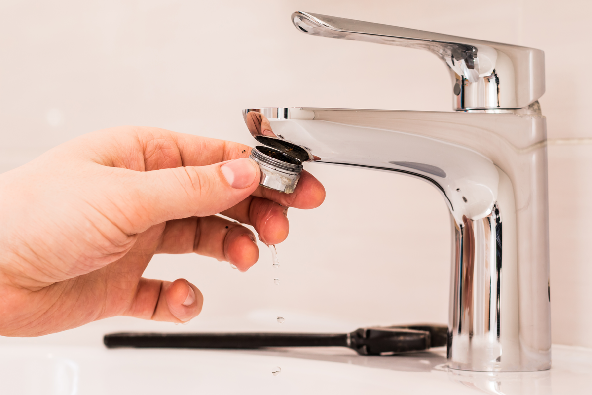 A person removing the aerator from a kitchen faucet in Syracuse, NY.